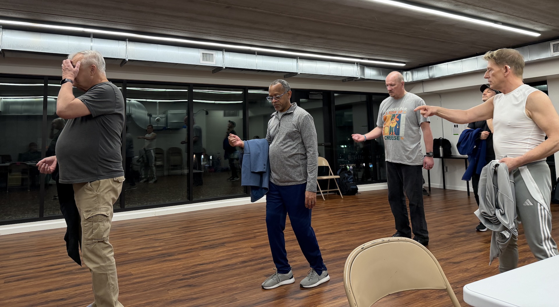 Teacher Rik Kutcher guides four men in a dance routine. The room is a dance studio.